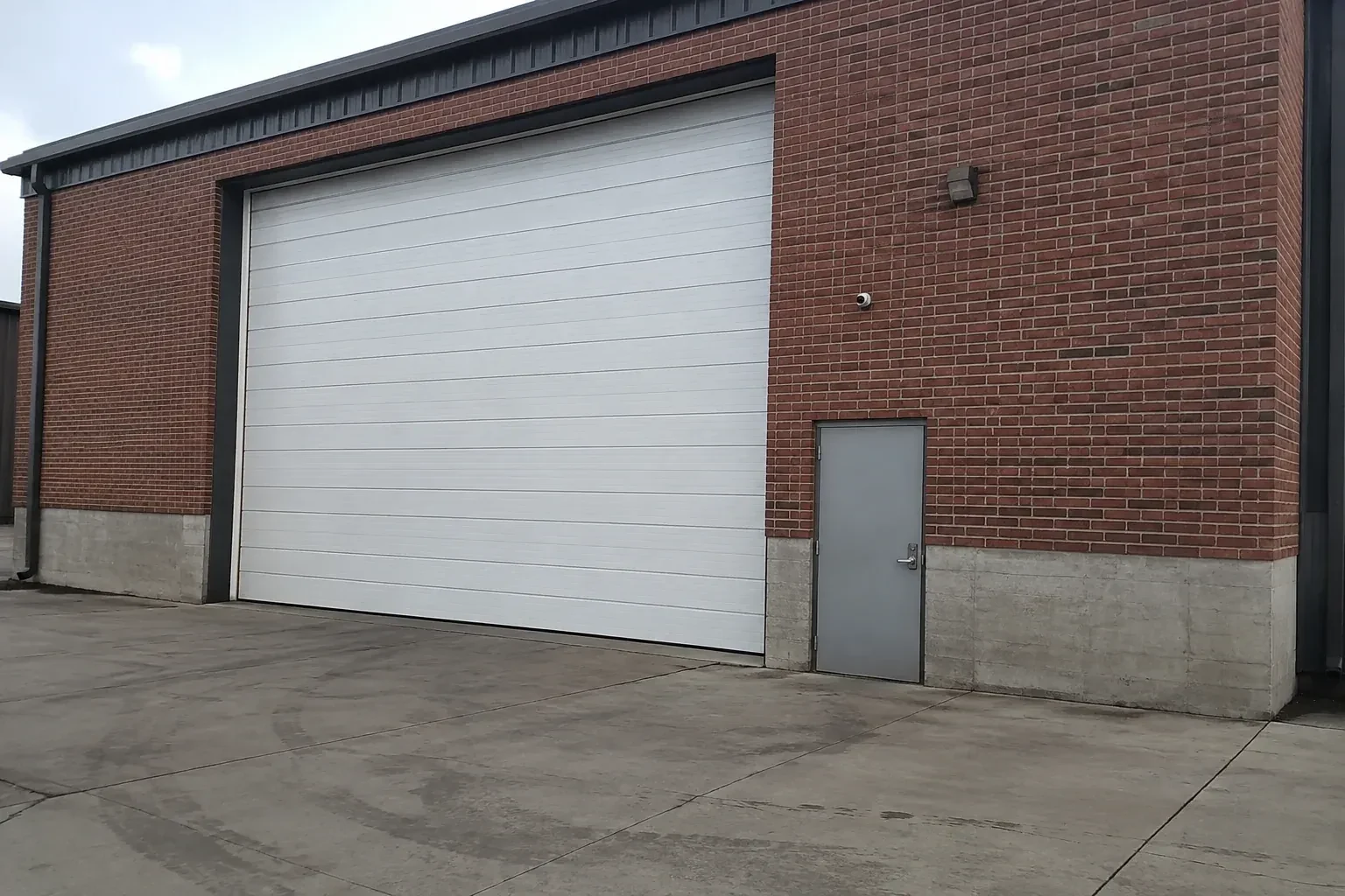 Tall closed sectional loading door beside a personnel door at a brick unit. — Commercial Sectional Door Repair, Markham